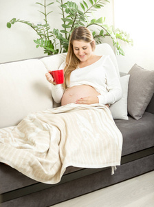 微笑孕妇放松在沙发上与杯茶