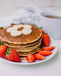 健康的早餐。草莓 香蕉 杯红茶白色背景用白色毛巾上煎饼