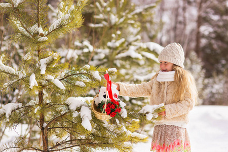 美丽可爱的小女孩带着礼物的圣诞树装饰冬季森林。树上有一篮子用鲜花和玩具