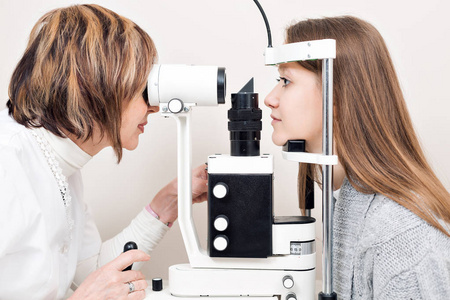 检查在私人诊所的年轻女人眼睛的高级女性验光师