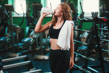 体育年轻女子饮料中的蛋白质鸡尾酒振动筛在健身房里。运动营养概念