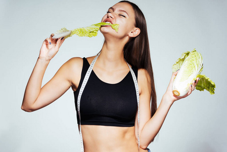 年轻的女运动手表她的身材，吃健康的低卡路里北京白菜