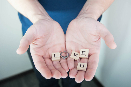 字母表字母木块瓷砖情人节爱的概念与结婚戒指在男子手中