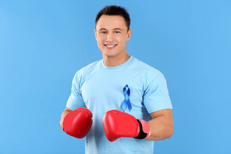 年轻男子在 tshirt 与蓝色丝带佩带拳击手套在颜色背景。前列腺癌认知概念