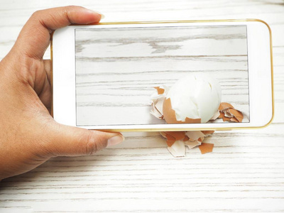 女用智能手机在木质背景下拍摄煮蛋照片