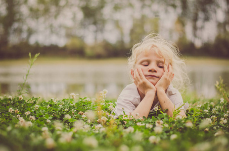 小可爱的女孩与金色的头发躺在草地上的河流放松