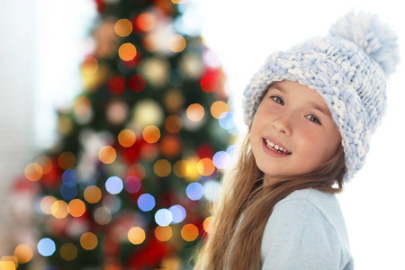 快乐的小女孩在帽子上对模糊的圣诞树