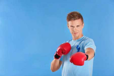 年轻男子在 tshirt 与蓝色丝带佩带拳击手套在颜色背景。前列腺癌认知概念