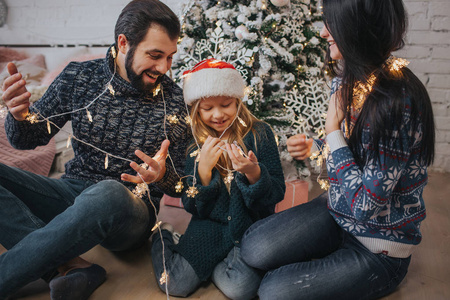 美丽的年轻家庭享受他们的假期时间在一起, 装饰圣诞树, 安排圣诞彩灯和有乐趣