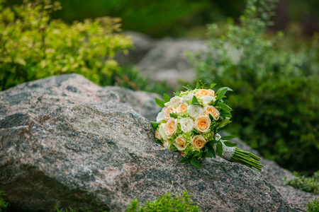 鲜花和绿叶的婚礼花束躺在一个绿色的背景岩石上。婚礼装饰品