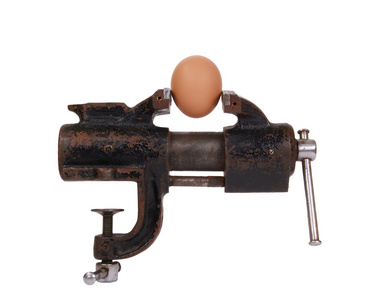 鸡蛋被困在旧生锈的金属制品虎钳上的白色背景