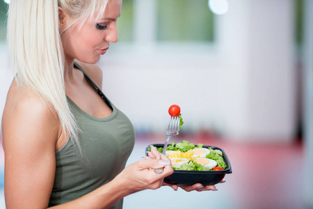 健康的年轻妇女吃蔬菜绿色沙拉在健身房