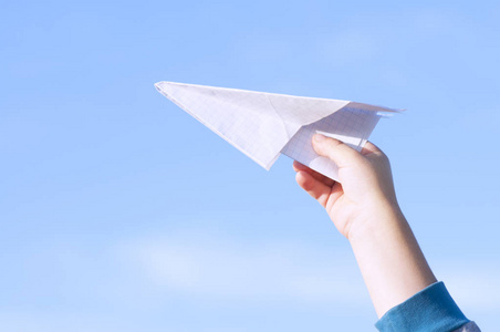 一个男孩玩玩具纸飞机领域在蓝天的衬托
