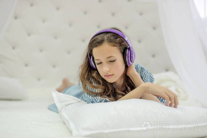 温柔天真的女孩听音乐, 戴着耳机躺在白色的床上