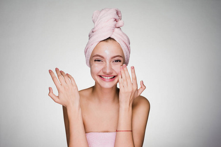 美丽的微笑的女孩在脸上敷上白色滋养霜, 头粉红色的毛巾