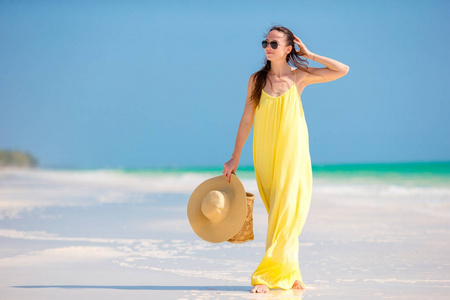在热带海滩假日的少妇在黄色礼服与帽子