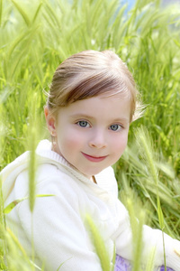 快乐的金发小女孩坐在绿色的尖峰草甸