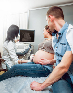 女医生和年轻孕妇与丈夫的病人。超声波设备。诊断.超声