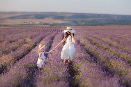 年轻美丽的母亲与可爱的女儿走在薰衣草领域在一个周末的一天, 在美妙的礼服和帽子