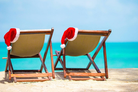 太阳躺椅与圣诞老人帽子在美丽的热带海滩, 白色的沙子和绿松石水。完美的圣诞假期