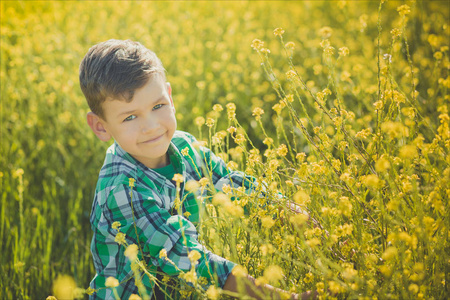 英俊快乐的男孩喜欢在田野上摆着夏天的黄色花朵穿乡村风格的衣服。可爱的孩子梦想未来的生活