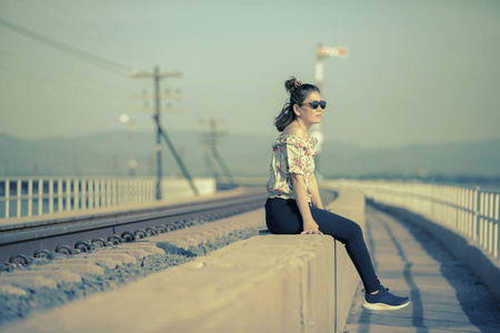 坐在铁轨旁的年轻女子戴着太阳眼镜