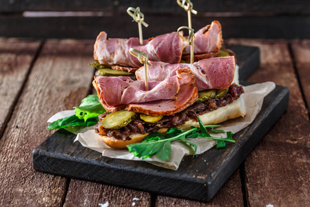 Delicius 三明治配烟熏猪肉黄瓜和洋葱在黑色木板上