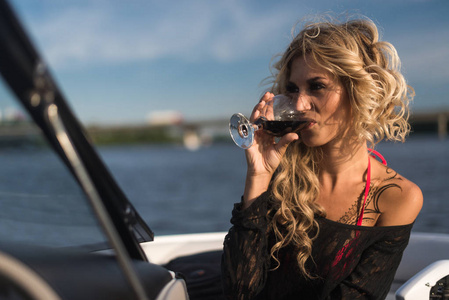 有魅力的女人轻松享受杯酒在蓝天大海户外的游艇上的肖像。享受和奢侈的生活方式