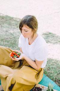 年轻的黑发妇女在野餐吃新鲜的草莓