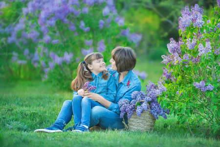 逗人喜爱的可爱的美丽母亲夫人妇女与黑发女孩女儿在淡紫色灌木的草甸。穿牛仔裤的人