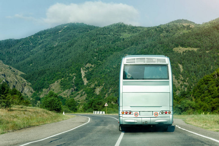 在绿色山脉之间的道路上的旅游巴士。后视图