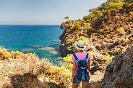 带背包的年轻女子旅行者站在悬崖边上, 望着地中海的风景, 夏日度假的概念