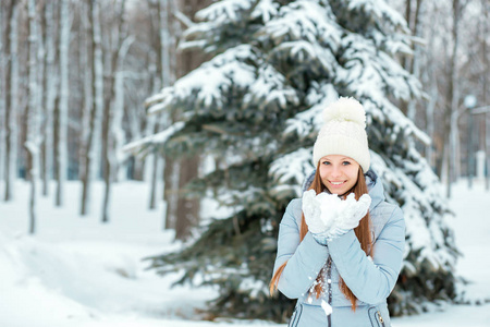 一个女孩穿着暖和的冬天的衣服和帽子在冬天的森林里吹雪, 水平。模型与美丽的微笑在圣诞树附近