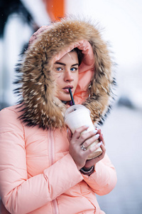 温暖的冬天夹克外面微笑的愉快的俏丽的妇女喜欢热的咖啡, 穿着手套和敞篷, 下雪天气