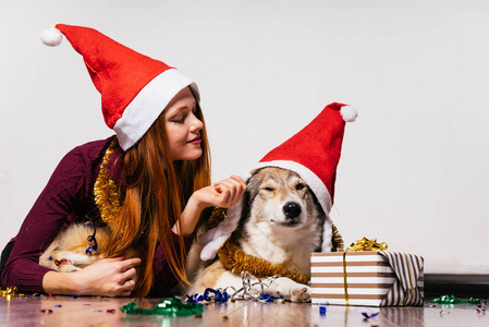 可爱的 redhaired 女孩, 她的头上有一个红色的新年帽躺在地板上与她的狗, 等待圣诞节