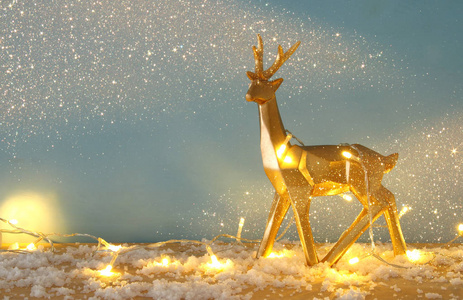 金色闪亮的驯鹿在白雪皑皑的木桌上圣诞花环灯