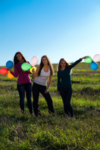 三个年轻漂亮的女人拿着气球进入田野，对抗