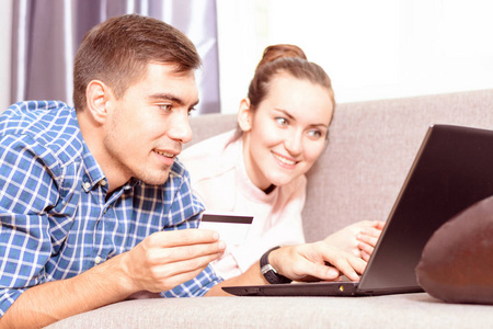 现代的年轻家庭用笔记本电脑在沙发上购买网上勒达, 用信用卡付款。情感面