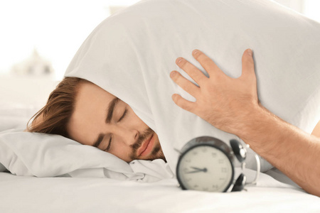 闹钟和年轻人试图睡在床上的枕头盖头