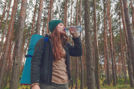 徒步旅行的女孩享受水。愉快的妇女游人与背包饮用水从瓶在自然