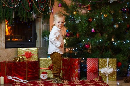 可爱的金发小男孩附近的壁炉和礼物圣诞树