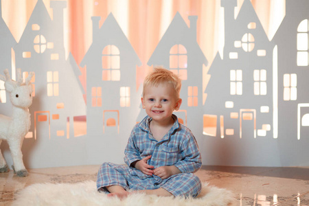 可爱的金发小男孩在睡衣附近的圣诞玩具纸房子