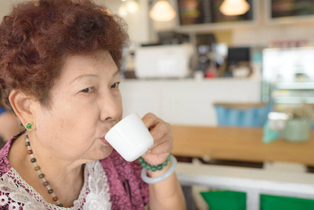 在咖啡馆喝一杯茶的亚洲高级妇女