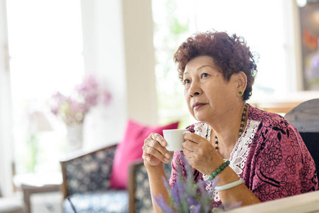 幸福的亚洲高级女人坐在家里喝茶。生活方式的概念