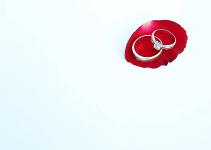 与复制空间在白色背景下的红玫瑰花瓣上的结婚戒指