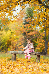 快乐的小女孩坐在长椅上笑着玩树叶。在大自然中, 漫步在空旷的空气中