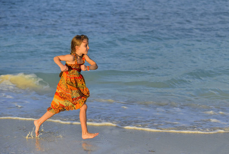 可爱的小女孩在日落的阳光下奔跑在海滩上。古巴