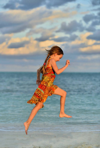可爱的小女孩在日落的阳光下奔跑在海滩上。古巴