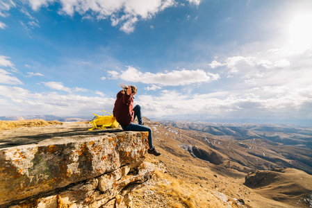 活跃的年轻女孩坐在悬崖边上的黄色背包, 享受自然