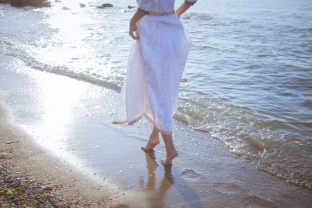 年轻的黑发女子打扮在清晨的夏日海滩美丽的白色礼服